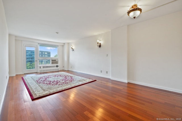 unfurnished living room featuring radiator heating unit, baseboards, and hardwood / wood-style floors