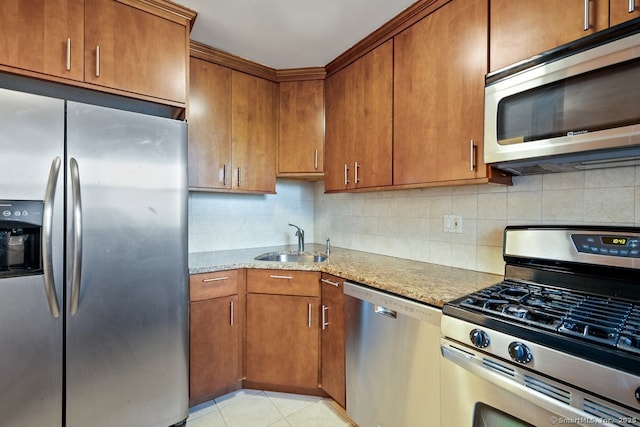 kitchen with tasteful backsplash, a sink, brown cabinets, stainless steel appliances, and light stone counters