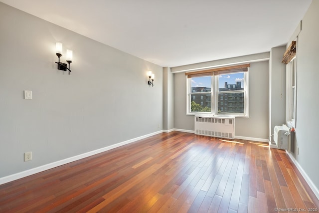 empty room featuring radiator heating unit, hardwood / wood-style flooring, and baseboards