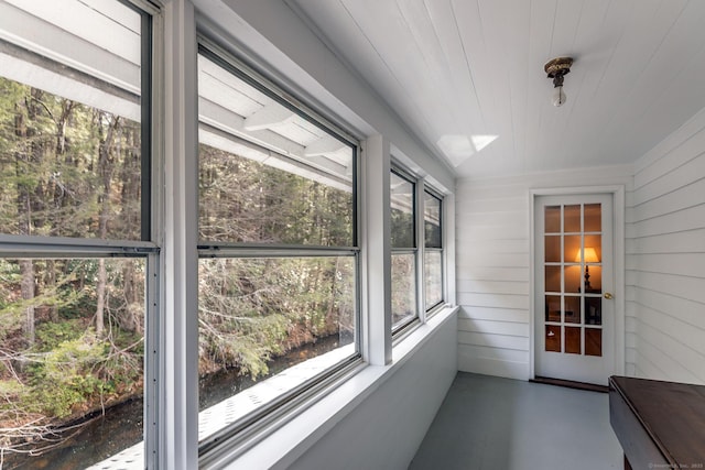unfurnished sunroom featuring wooden walls, a water view, and finished concrete floors