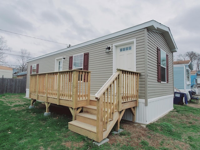 rear view of house featuring a wooden deck, fence, and a lawn