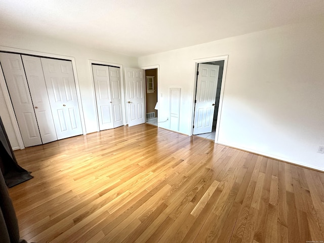 unfurnished bedroom with two closets, visible vents, and light wood finished floors