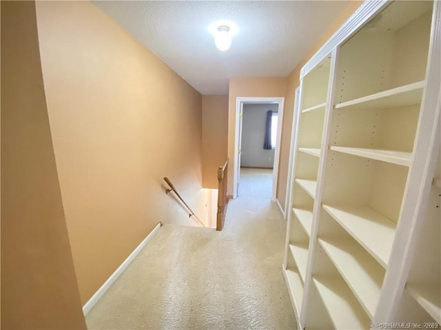 hall featuring carpet flooring, baseboards, and an upstairs landing