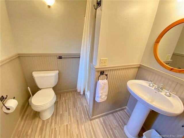 bathroom featuring curtained shower, a wainscoted wall, wood finished floors, toilet, and a sink