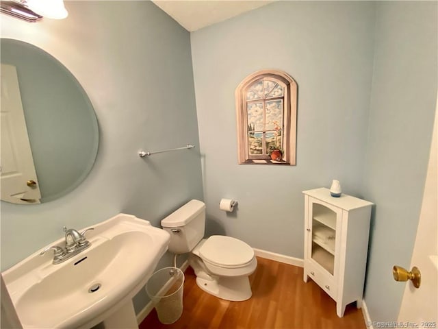 bathroom featuring baseboards, wood finished floors, a sink, and toilet