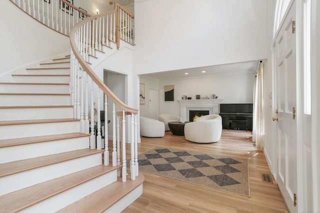 foyer featuring stairway, a high ceiling, wood finished floors, visible vents, and a lit fireplace