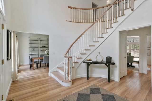 stairs featuring wood finished floors, a towering ceiling, and baseboards