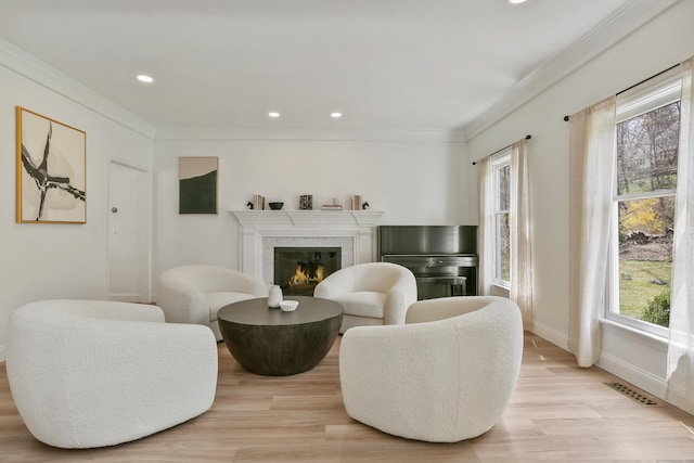 living area with light wood-style flooring, visible vents, recessed lighting, a premium fireplace, and crown molding