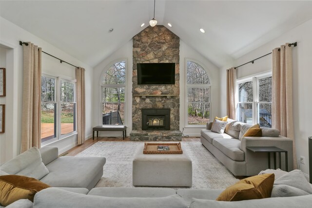 living area featuring high vaulted ceiling, a stone fireplace, wood finished floors, and recessed lighting