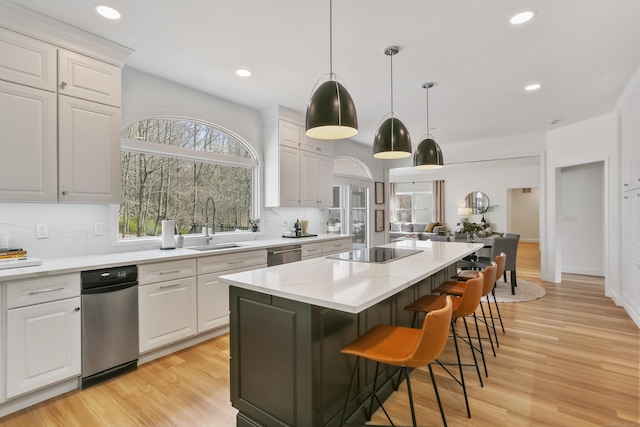 kitchen featuring a center island, stainless steel dishwasher, a sink, black electric stovetop, and light countertops