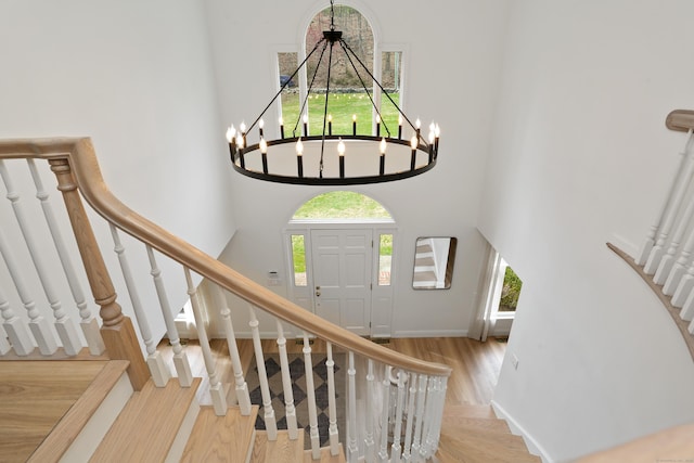 entryway featuring stairway, wood finished floors, an inviting chandelier, a towering ceiling, and baseboards