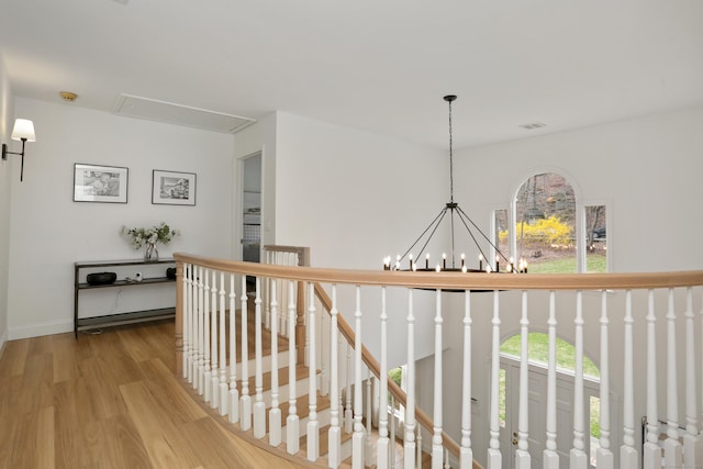 hall with attic access, wood finished floors, a healthy amount of sunlight, and a notable chandelier
