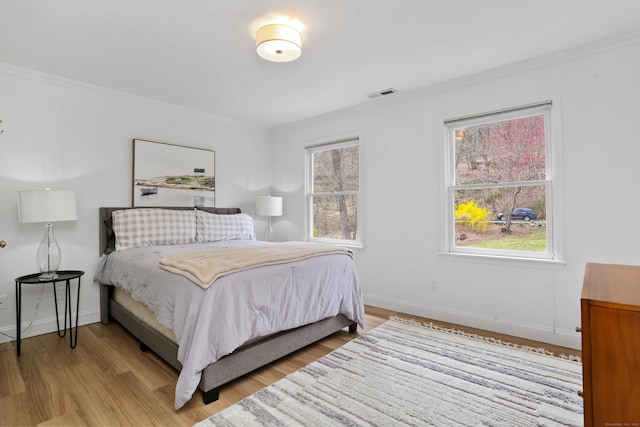 bedroom featuring light wood-type flooring, visible vents, baseboards, and ornamental molding