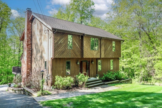 view of front facade with a chimney, a front lawn, and roof with shingles