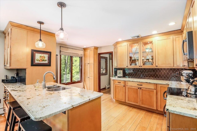 kitchen with a sink, stainless steel appliances, light wood-style floors, tasteful backsplash, and a breakfast bar area