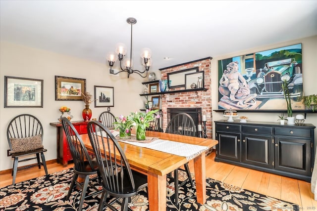 dining room featuring a chandelier, light wood finished floors, a brick fireplace, and baseboards