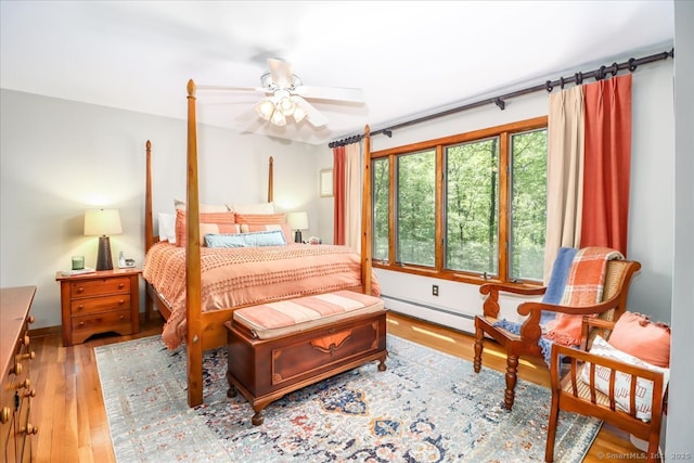 bedroom featuring a baseboard heating unit, wood finished floors, and ceiling fan