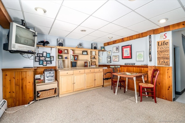 dining space featuring a paneled ceiling, light carpet, a baseboard heating unit, wood walls, and wainscoting