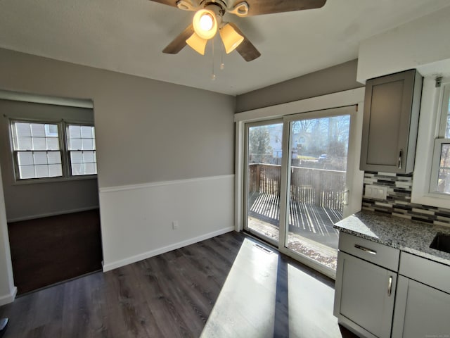 unfurnished dining area featuring baseboards, a ceiling fan, and dark wood-style floors