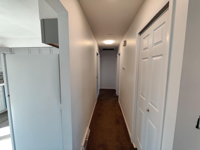 corridor with baseboards, visible vents, and dark carpet