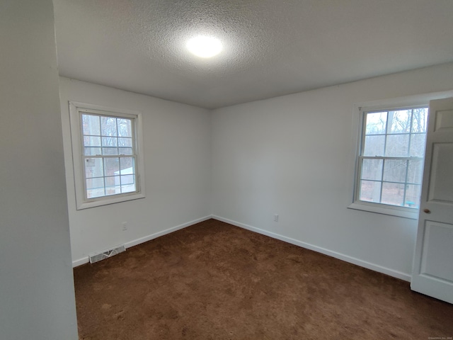 spare room with dark carpet, baseboards, visible vents, and a textured ceiling