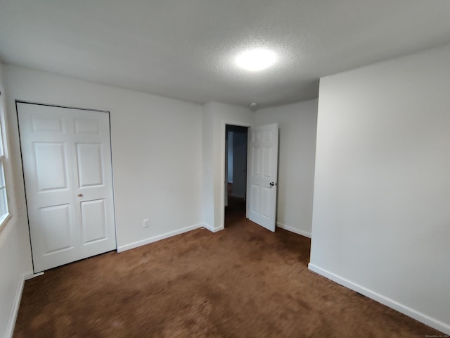 unfurnished bedroom with dark carpet, a textured ceiling, and baseboards