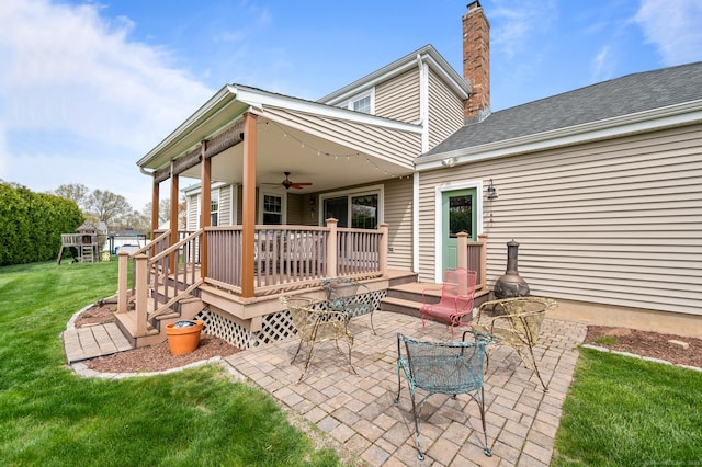 back of property with ceiling fan, a deck, a chimney, a patio, and a yard