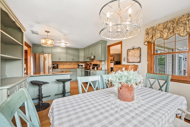 dining space with an inviting chandelier, light wood-style flooring, and visible vents
