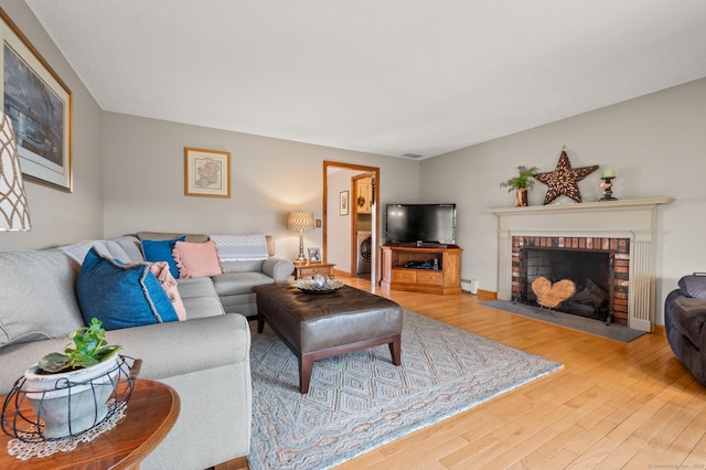 living area featuring a baseboard radiator, washer / dryer, wood finished floors, and a fireplace