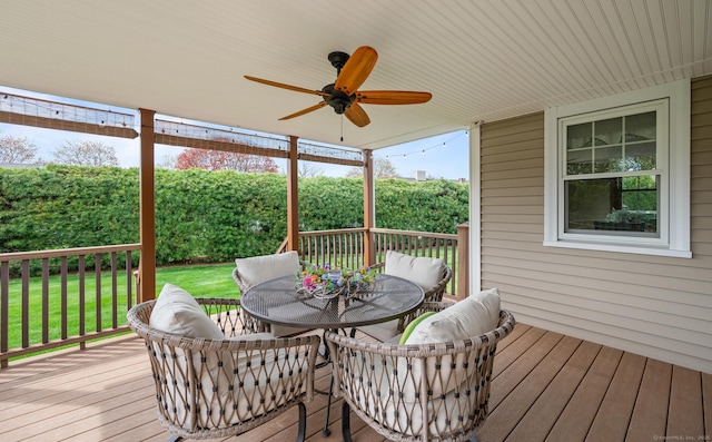 wooden deck featuring outdoor dining area, a ceiling fan, and a lawn