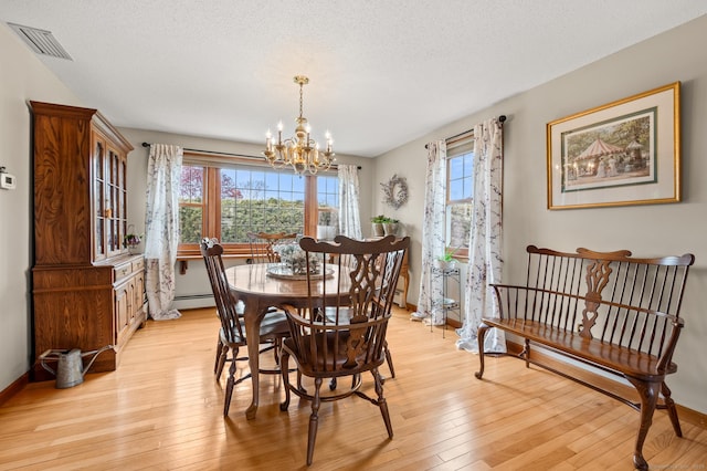 dining room with an inviting chandelier, visible vents, light wood-style flooring, a wealth of natural light, and a baseboard heating unit