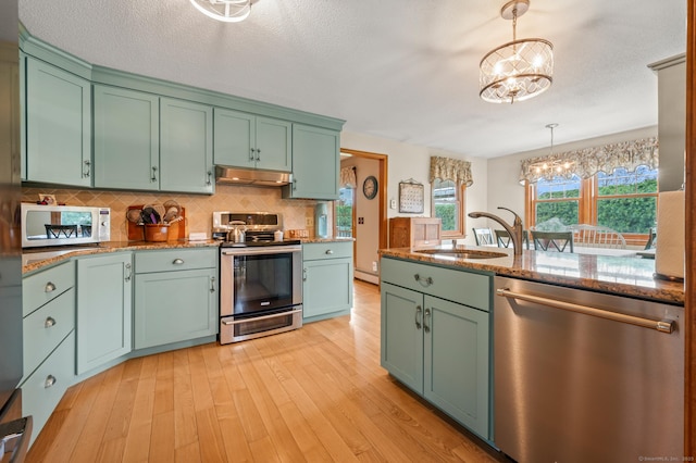 kitchen with a sink, green cabinetry, appliances with stainless steel finishes, and a notable chandelier