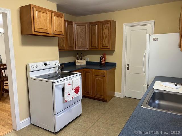 12 Homecrest St, Newington, CT 06111 - kitchen with white appliances, a sink, brown cabinetry, dark countertops, and light floors