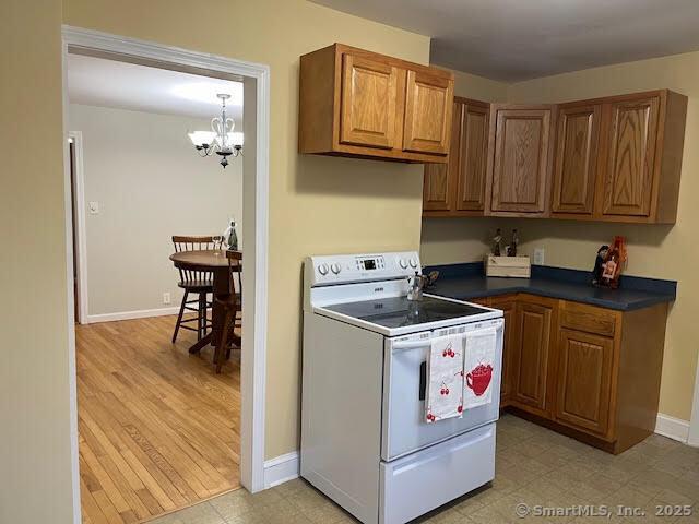 12 Homecrest St, Newington, CT 06111 - kitchen with white electric stove, dark countertops, brown cabinets, a chandelier, and baseboards