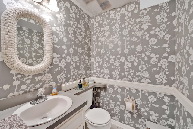 half bathroom with toilet, wallpapered walls, and vanity