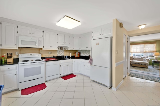 kitchen with a sink, dark countertops, white cabinets, and white appliances