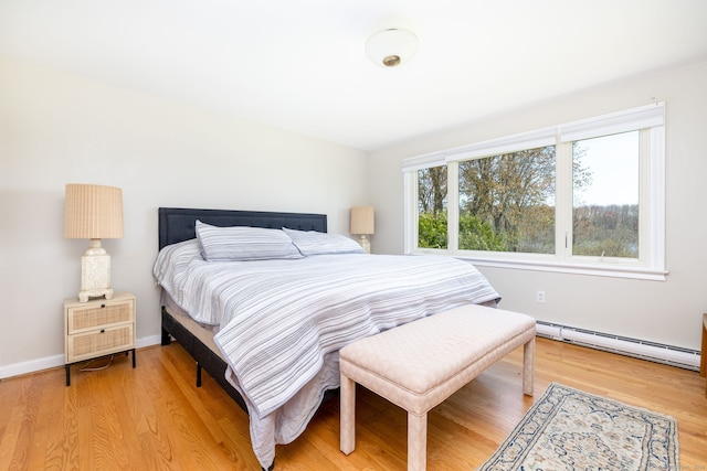 bedroom featuring light wood-style flooring, a baseboard heating unit, and baseboards