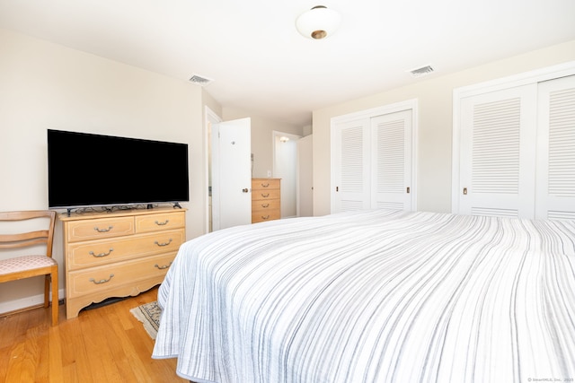 bedroom featuring visible vents, light wood finished floors, and two closets