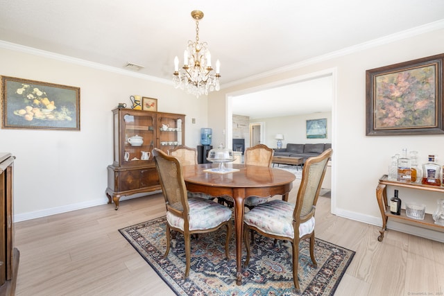 dining space featuring light wood-style flooring, a chandelier, ornamental molding, baseboards, and visible vents