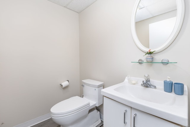 bathroom with a drop ceiling, toilet, vanity, and baseboards