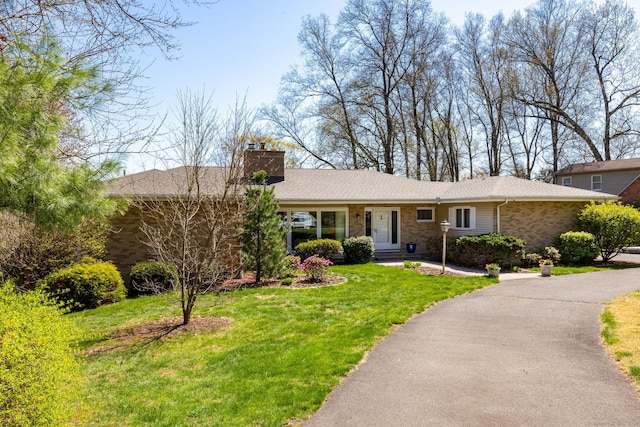 ranch-style house featuring a front lawn, a chimney, and brick siding