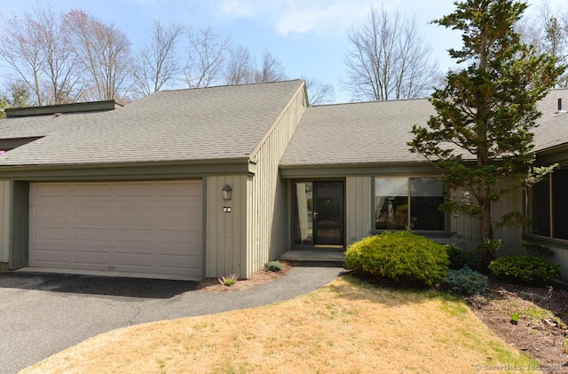 view of front facade featuring an attached garage, a front lawn, driveway, and roof with shingles
