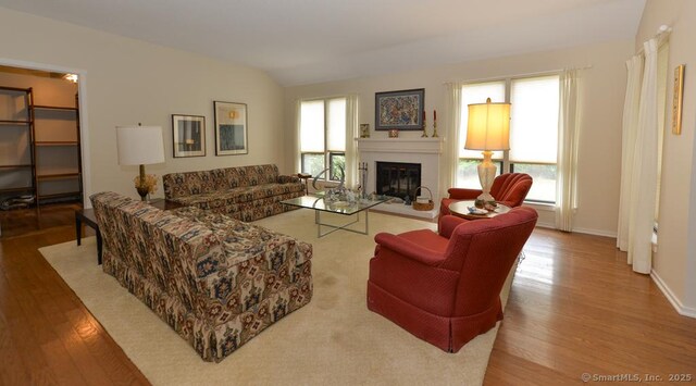 living room with a glass covered fireplace, vaulted ceiling, wood finished floors, and baseboards