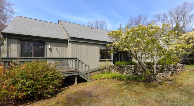 rear view of property with a wooden deck, roof with shingles, and a lawn