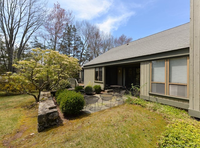 rear view of house featuring a lawn, roof with shingles, and a patio