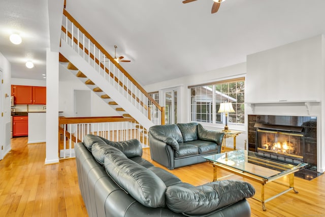 living room with stairs, a fireplace, baseboards, light wood-type flooring, and a ceiling fan