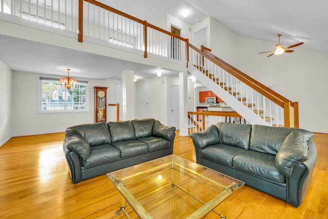 living room with light wood-style floors, stairs, ceiling fan with notable chandelier, and high vaulted ceiling