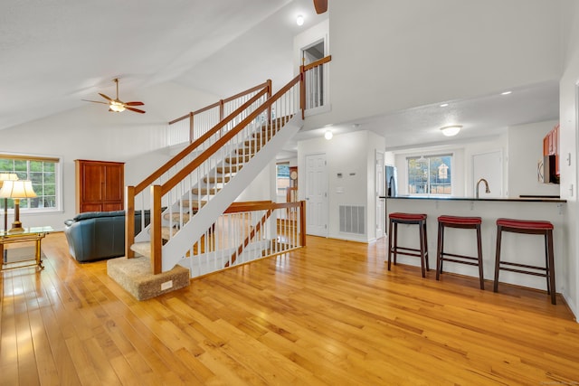 living room featuring a ceiling fan, high vaulted ceiling, visible vents, and light wood-type flooring