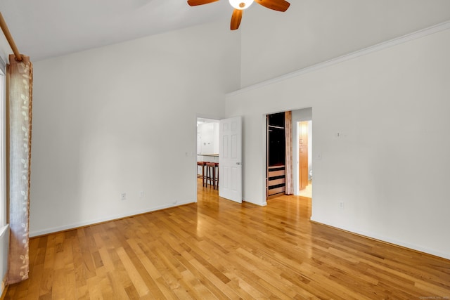 interior space with a ceiling fan, high vaulted ceiling, baseboards, and light wood-style floors