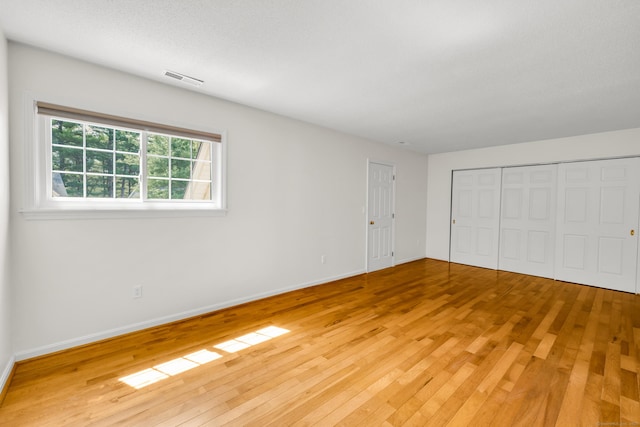 unfurnished bedroom featuring light wood-style floors, baseboards, a closet, and visible vents